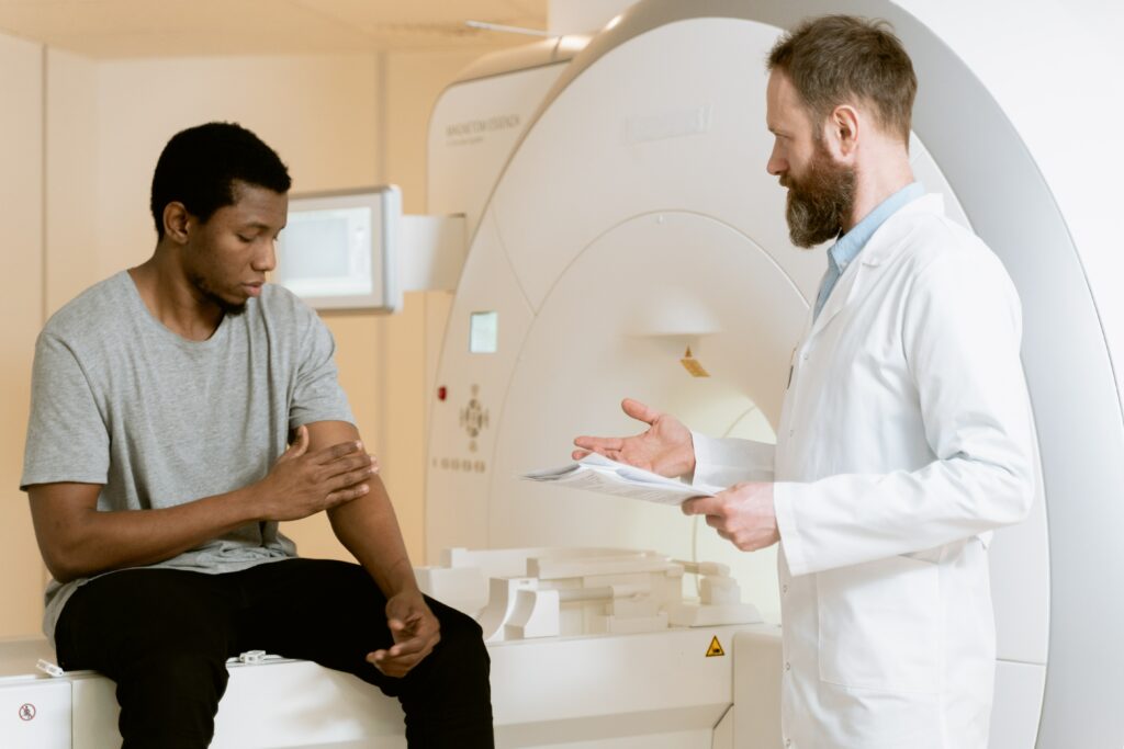 A cancer patient sits on an MRI bed while his doctor tells him about the Patient Resource