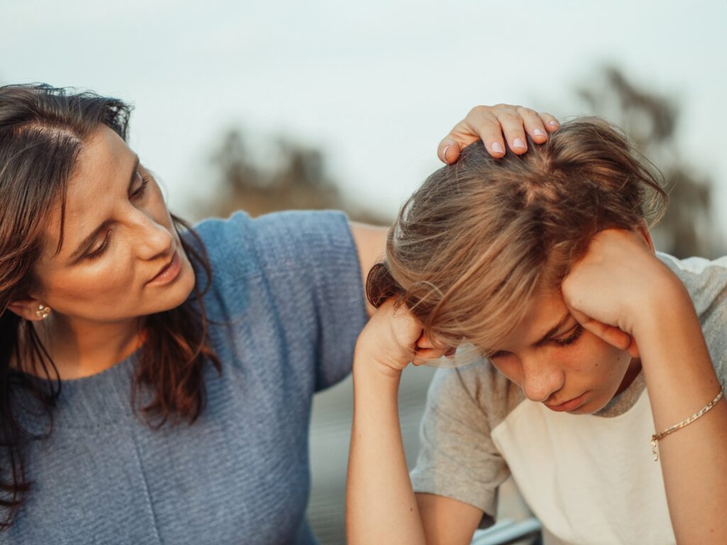 Mom comforting teenage son displaying a typical grief reactions in children of his age.