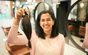 Portrait of a smiling young woman holding up her cut ponytail after getting her hair done at a salon.