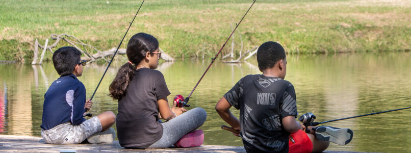 Three kids sit on a dock fishing at Reel Connection.