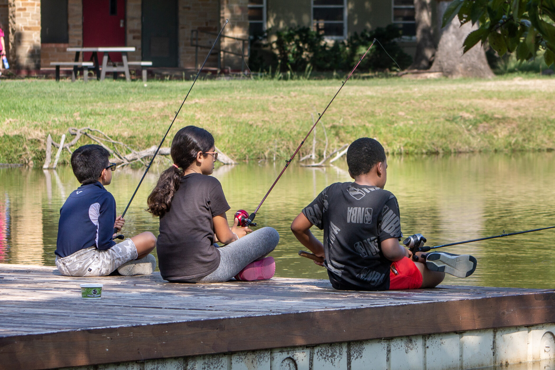 Three kids sit on a dock fishing at Reel Connection.