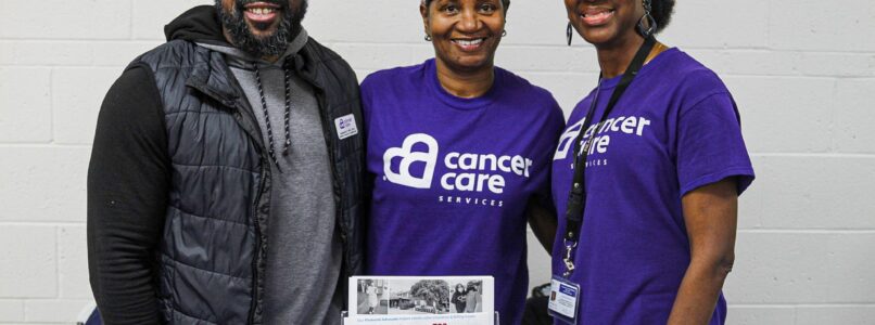 Three members of Cancer Care Services' community outreach team stand behind a table at a health screening event.