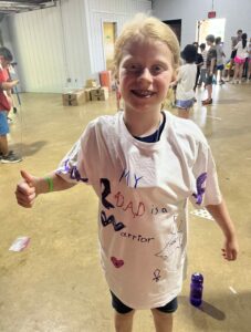 A young girl at CampCARE 2023 shows the front of her decorated t-shirt.