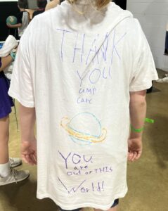 A young girl at CampCARE 2023 shows the back of her decorated t-shirt.