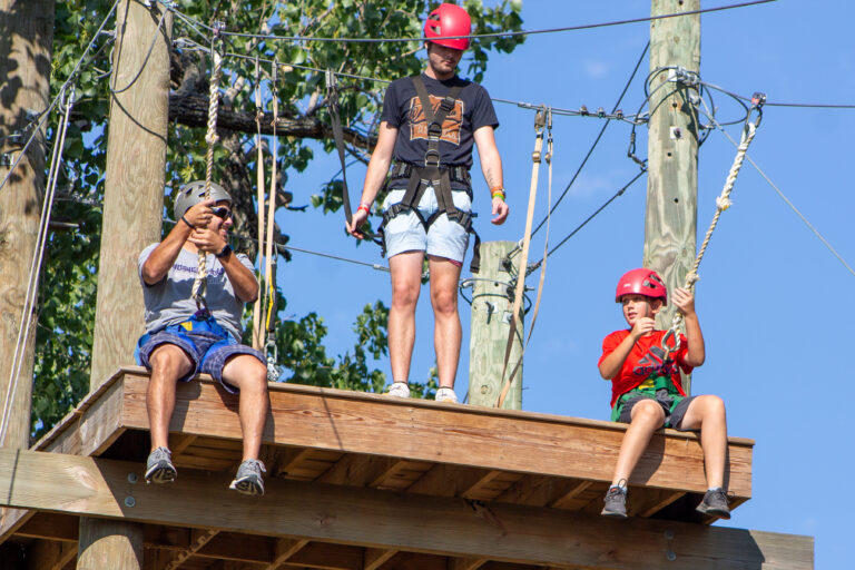 A father and son sit at the top of the zipline at Camp Connect.