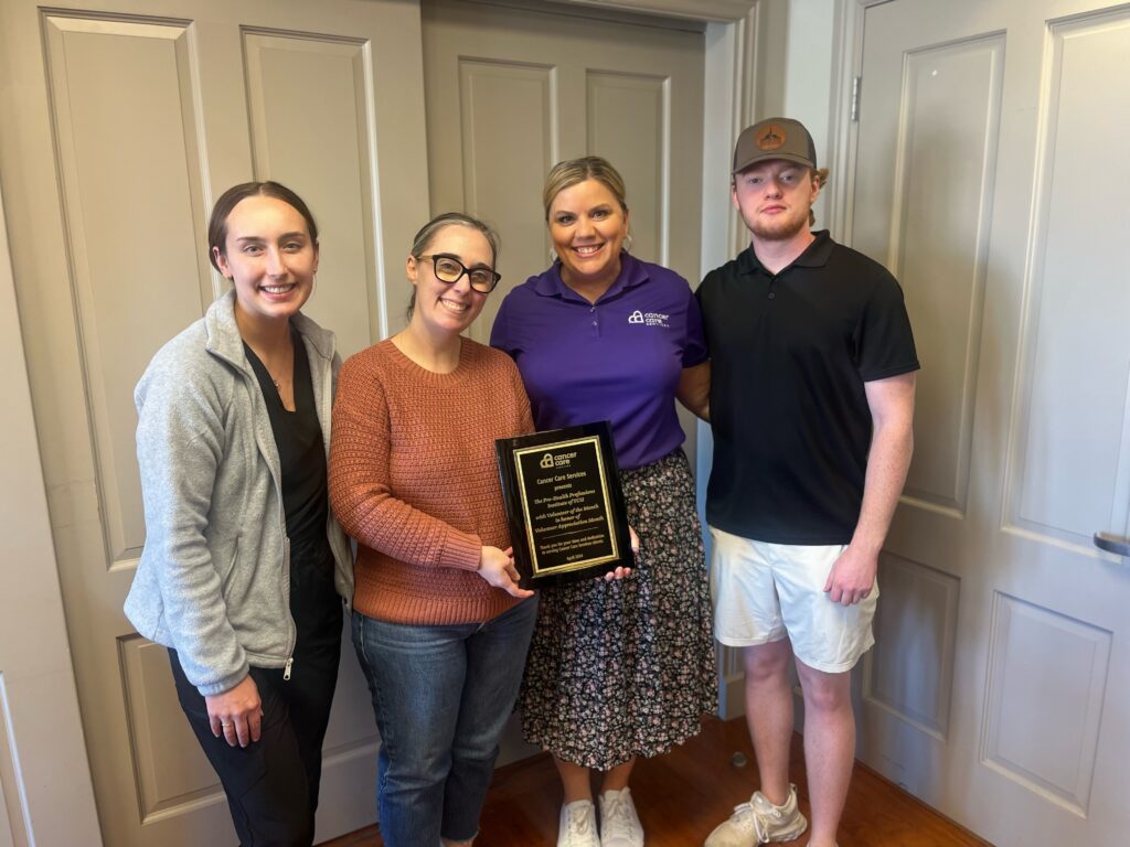 Two women and one man from the TCU Pre-Health Institute pose with a Cancer Care Services' staff member while holding an award for National Volunteer Month.