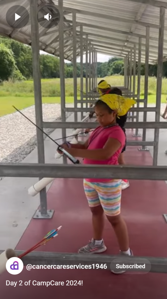 A young girl stands in an archery range preparing her bow and arrow at CampCARE 2024.