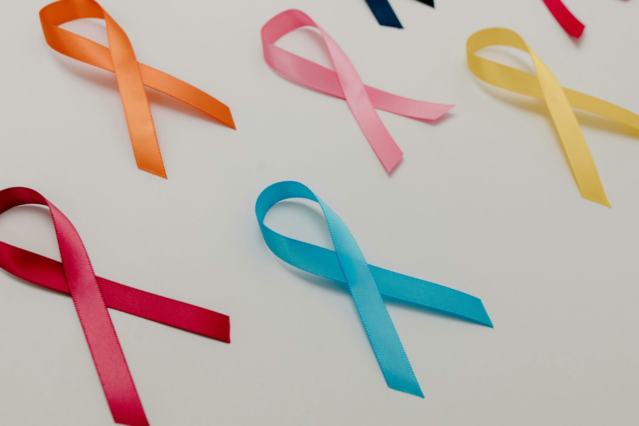 Red, blue, orange, pink, and yellow cancer ribbons are laid on a white surface.