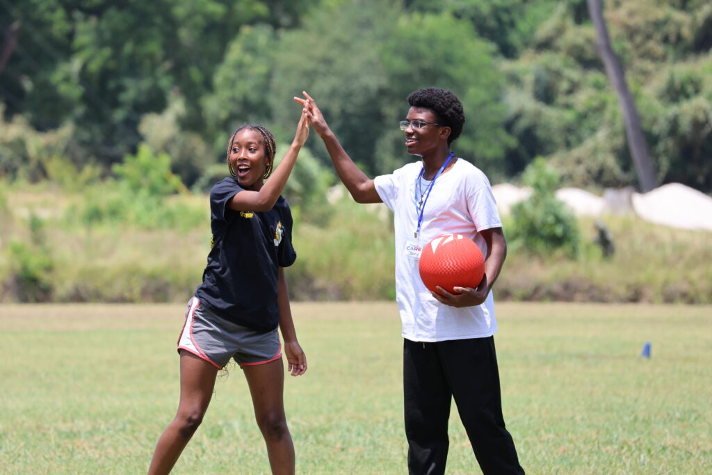 A teenage girl and boy high five while playing kickball at Teen Retreat 2024.