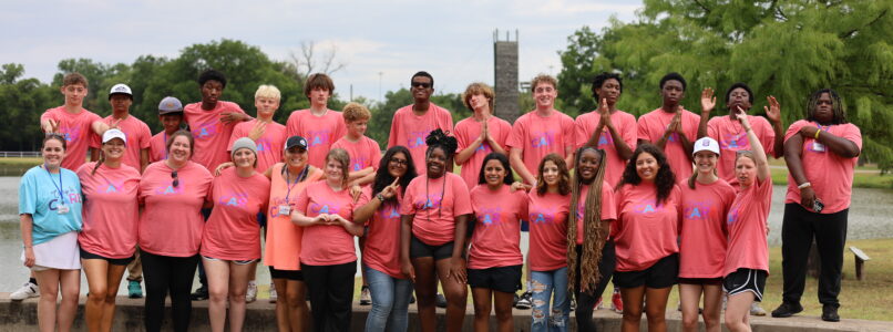 A diverse group of teenagers pose in front of a lake at Cancer Care's Teen Retreat 2024.